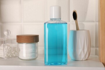 Bottle of mouthwash, toothbrush, cotton buds and pads on white shelf in bathroom