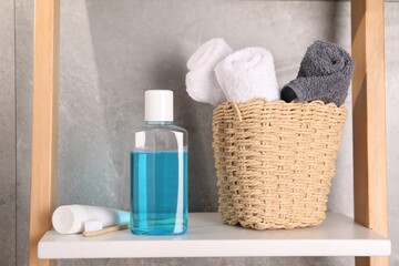 Bottle of mouthwash, toothpaste, toothbrush and towels on shelf in bathroom