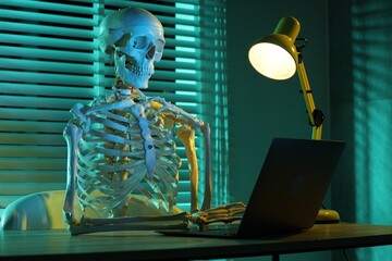 Waiting concept. Human skeleton sitting at wooden table with laptop indoors