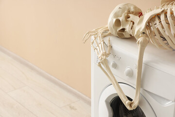 Waiting concept. Human skeleton lying on washing machine near beige wall indoors, space for text
