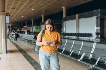 Happy Caucasian Woman waiting at Flight Gates for Plane Boarding, Uses Mobile Smartphone. 30s female Checking Trip Destination on Internet, concept of traveling