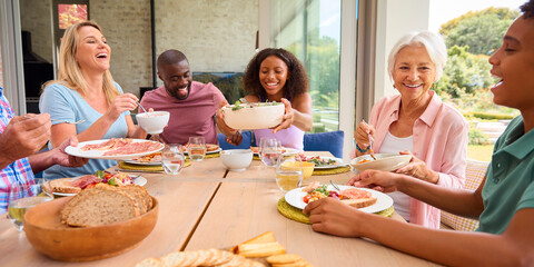 Three Generation Family Indoors Around Table At Home Serving And Eating Meal Together