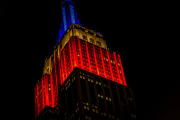 Stunning view of the top of a  Empire State Building skyscraper illuminated in red and blue, rising...