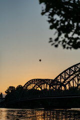 Obraz premium hot balloon in the evening sunset time flying above the city and the bridge