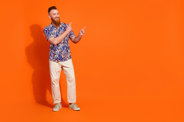 Full size photo of cheerful man with red long beard wear stylish shirt indicating at sale empty space isolated on orange color background