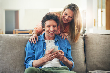 Mature, couple and happy on couch with phone for reading online news, social media scroll and embrace in home. People, hug and laughing with smartphone for funny meme, bingo or digital gaming on sofa