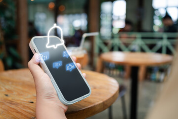 Hand holding smartphone showing notification with bell symbol, chat messages, emails, and social...