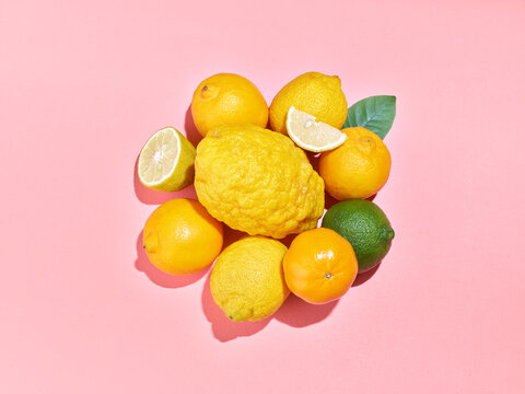 Fruits frais de la M&eacute;diterran&eacute;e, agrumes dispos&eacute;s sur fond rose avec c&eacute;drat, citron vert, citron jaune, bergamote, demi citron coup&eacute; et quartier de citron, lumi&egrave;re solaire, 