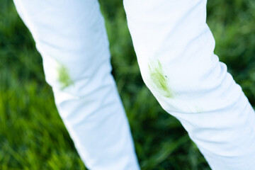 Close up dirty grass stains on white clothes. An unrecognizable person with green knees on a green background. Spoiled clothes