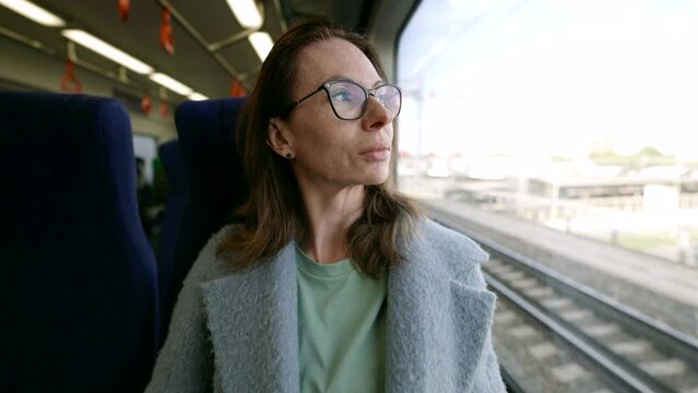 A charming middle-aged woman, wearing glasses, enjoys a moment of travel on public transport, embodying an atmosphere of coziness and comfort.