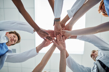 Doctor, hands together and below with team for meeting, unity or motivation at hospital. Low angle or closeup of medical group piling or touching in collaboration, solidarity or mission at clinic