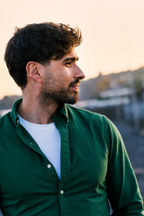 Portrait of a young man in a casual green shirt, captured in profile during the golden hour, with soft background blur emphasizing his thoughtful expression.