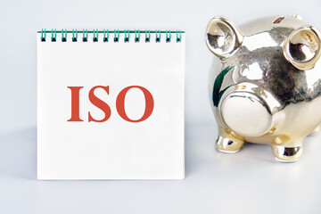 ISO. International Organization for Standardization. A Word ISO on a vertically standing notebook near the piggy bank on a light background