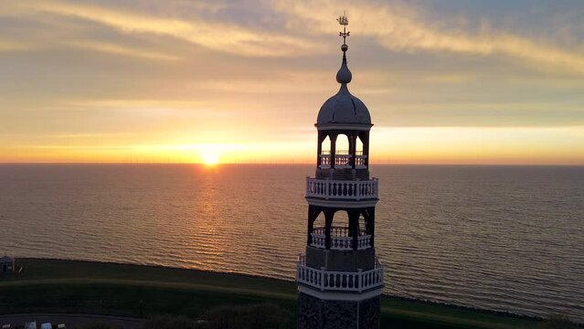 Aerial drone footage of historic small city of Hindeloopen, Hylpen with dike, seawall, next to IJsselmeer lake with iconic church and village during spectacular sunset
