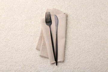 Stylish cutlery and dinner napkin on beige textured table, top view