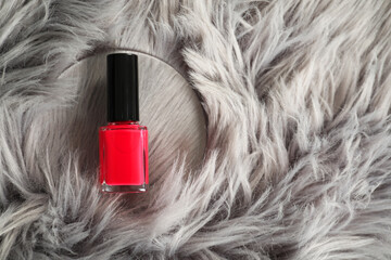 Bright nail polish in bottle on grey faux fur, top view. Space for text