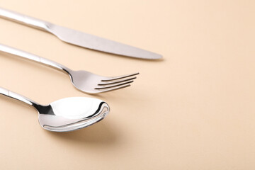 Stylish silver cutlery set on beige background, closeup. Space for text