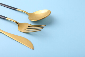 Stylish golden cutlery set on light blue background, closeup. Space for text