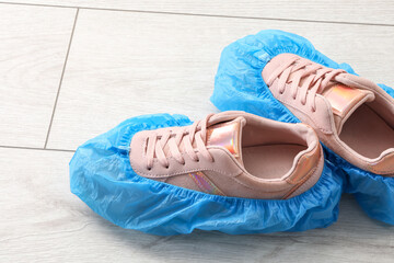 Women`s sneakers in blue shoe covers on light wooden floor