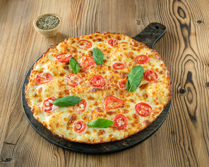 Cheese and sausage pizza with basil and tomatoes on a wooden floor