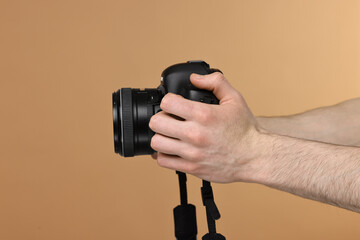 Photographer holding camera on beige background, closeup. Space for text