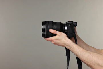 Photographer holding camera on grey background, closeup. Space for text