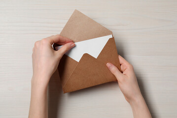 Woman taking card out of letter envelope at light wooden table, top view