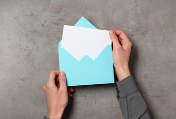 Woman holding letter envelope with card at grey textured table, top view