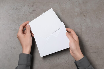 Woman taking card out of letter envelope at grey textured table, top view