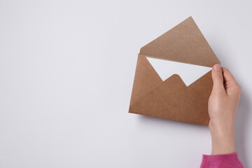 Woman holding letter envelope with card at white table, top view. Space for text