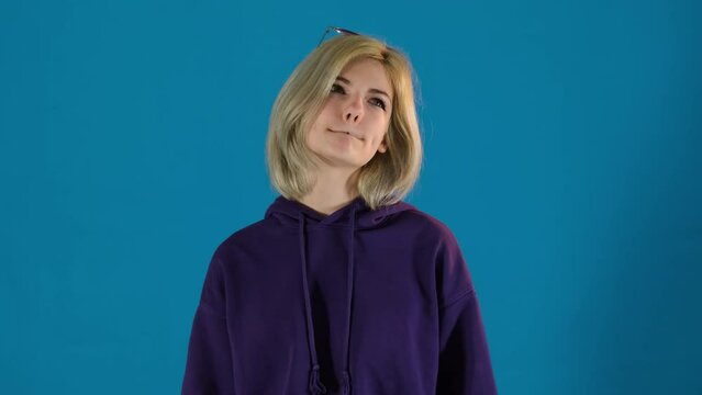 Teenager squints thinking about problem on blue background. Young lady looks down exploring different avenues for solution