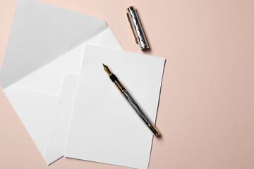 Blank sheet of paper, letter envelope and pen on beige background, top view. Space for text