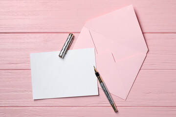 Blank sheet of paper, pen and letter envelope on pink wooden table, top view. Space for text