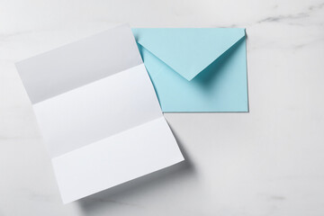 Blank sheet of paper and letter envelope on white marble table, top view