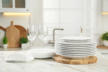 Clean plates, glasses and butter dish on white marble table in kitchen