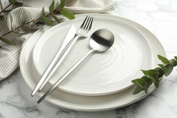 Stylish setting with cutlery, napkin, eucalyptus branches and plates on white marble table, closeup