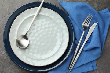 Stylish setting with cutlery, plates and napkin on grey textured table, flat lay