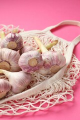 String bag with garlic heads on bright pink background, closeup