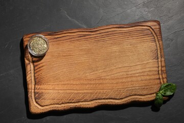 Wooden cutting board and spices on dark gray textured table, top view. Space for text