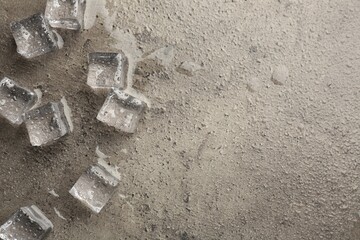Melting ice cubes and water drops on grey textured table, flat lay. Space for text