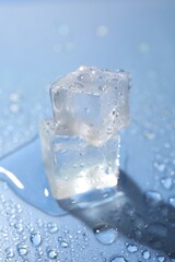 Melting ice cubes and water drops on light blue background, closeup