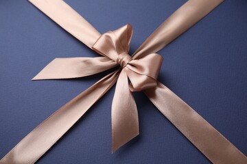 Fototapeta premium Beige satin ribbon with bow on blue background