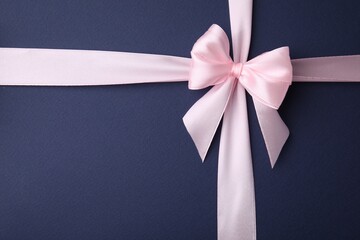 Pink satin ribbon with bow on blue background, top view