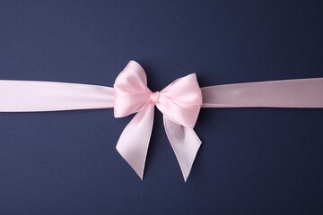 Pink satin ribbon with bow on blue background, top view