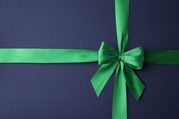 Green satin ribbon with bow on blue background, top view