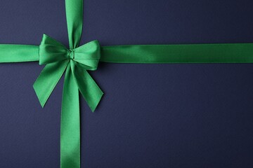 Green satin ribbon with bow on blue background, top view