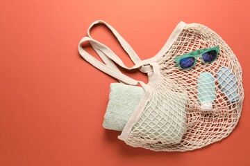 String bag, sunglasses, cosmetic products and towel on coral background, top view. Space for text