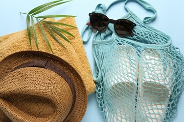 String bag, different beach accessories and palm leaf on light blue background, flat lay