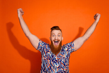 Photo of cheerful funky guy dressed print shirt yelling yeah rising fists isolated orange color...