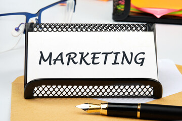 A word MARKETING the inscription on the business card on the table near the pen, a calculator, a stand with a ticker